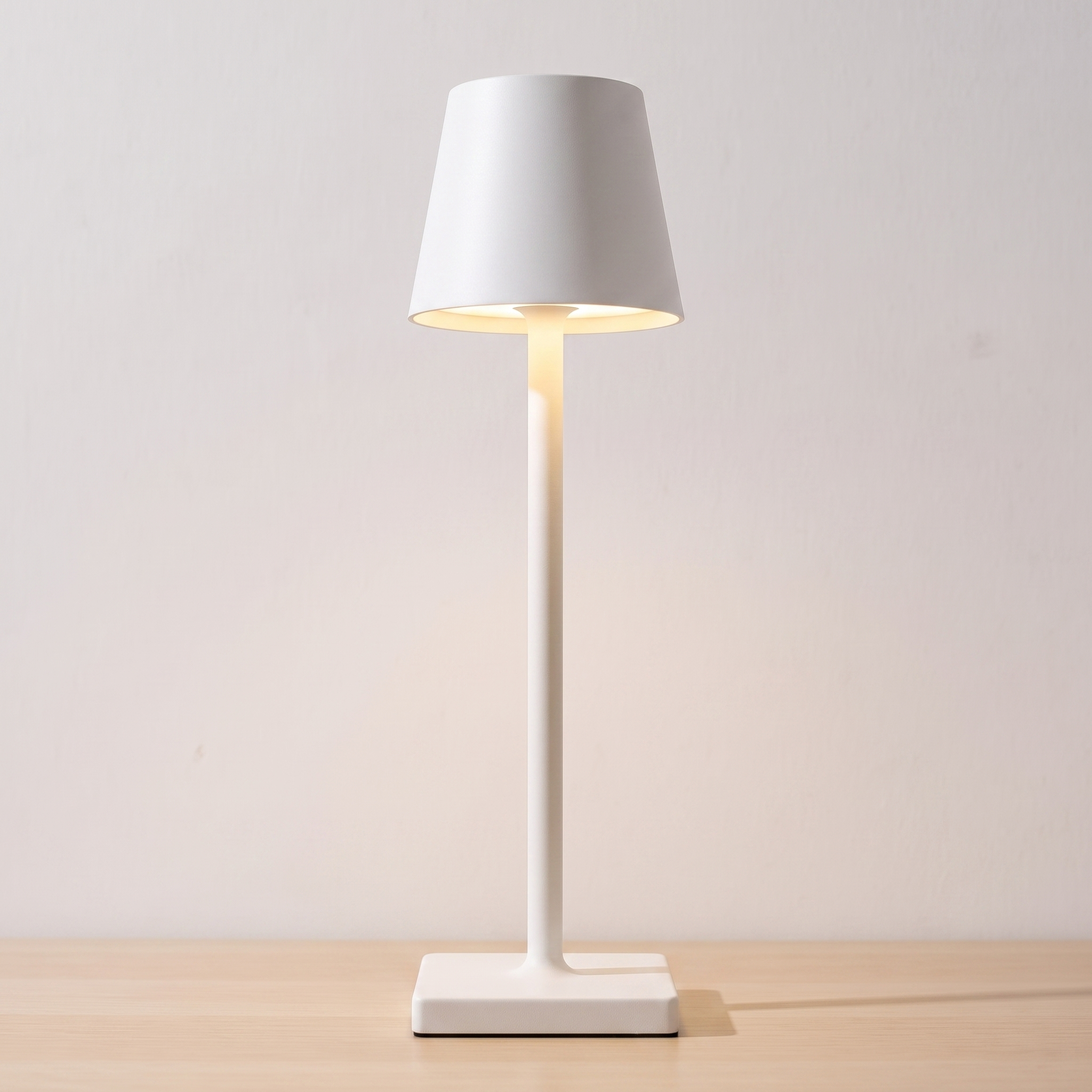 Lámpara de mesa recargable sin cable Nomad en blanco, encendida sobre una mesa de roble