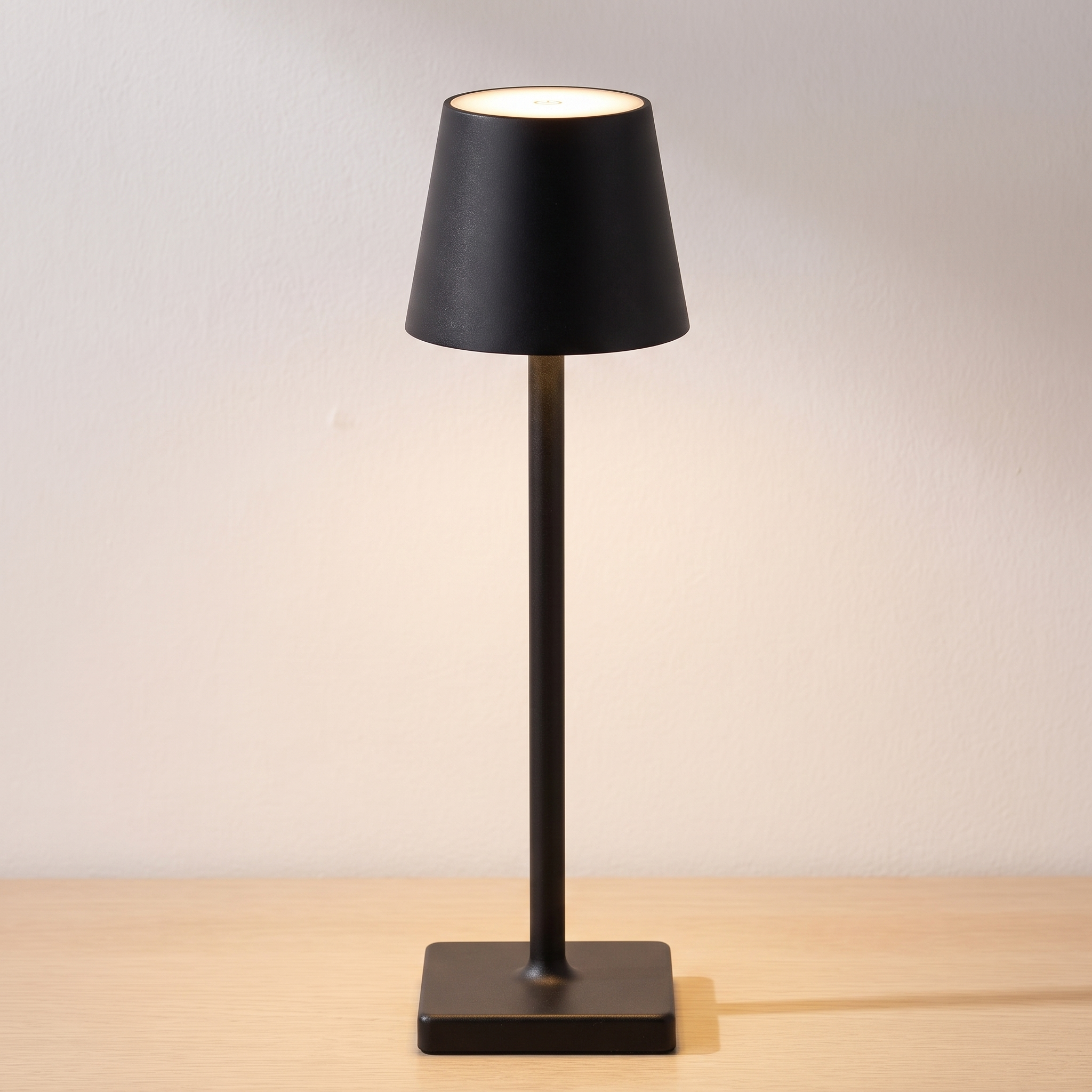 Lámpara de mesa recargable sin cable Nomad en negro, encendida sobre una mesa de roble