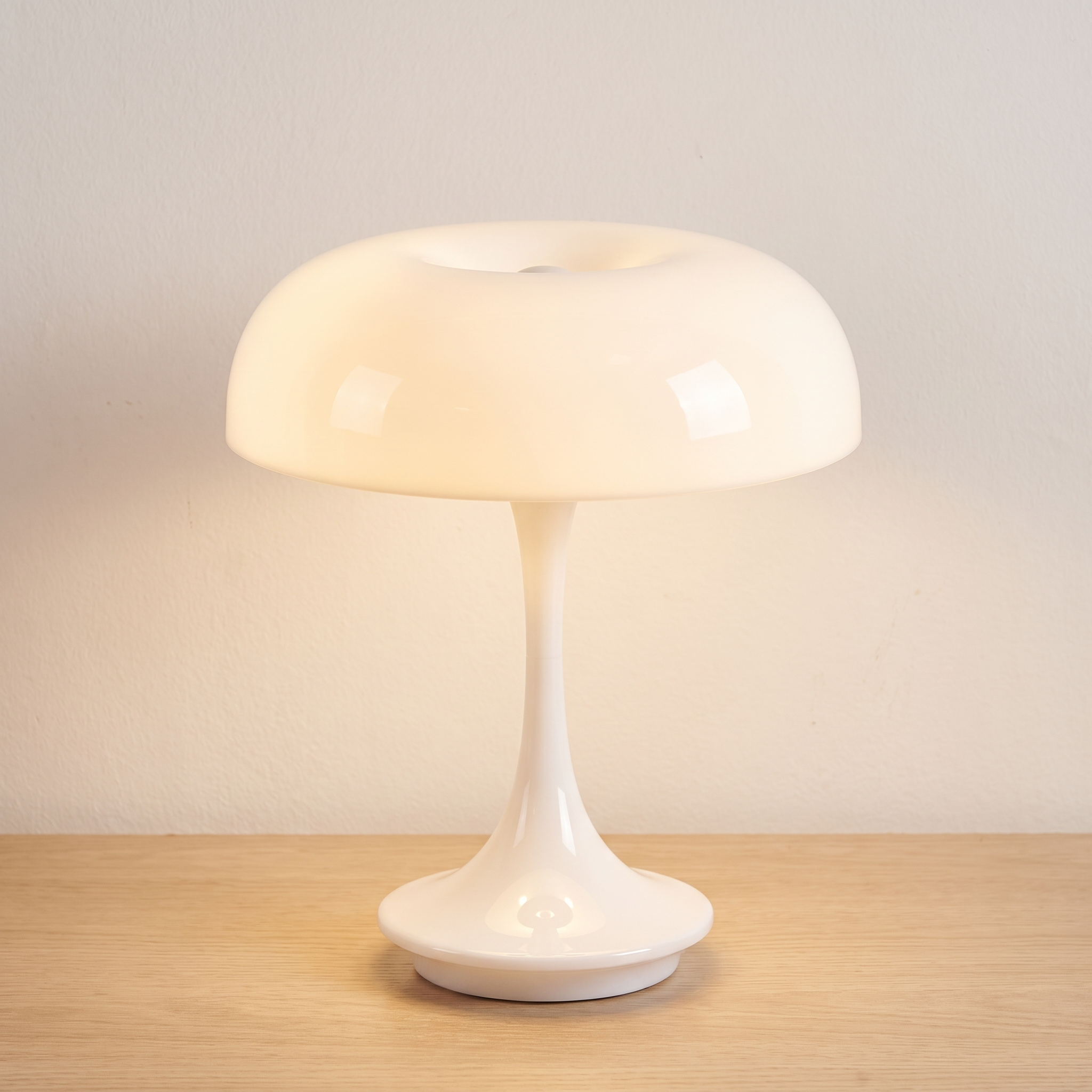 Lámpara de mesa seta Mila en blanco brillante, encendida sobre una superficie de roble