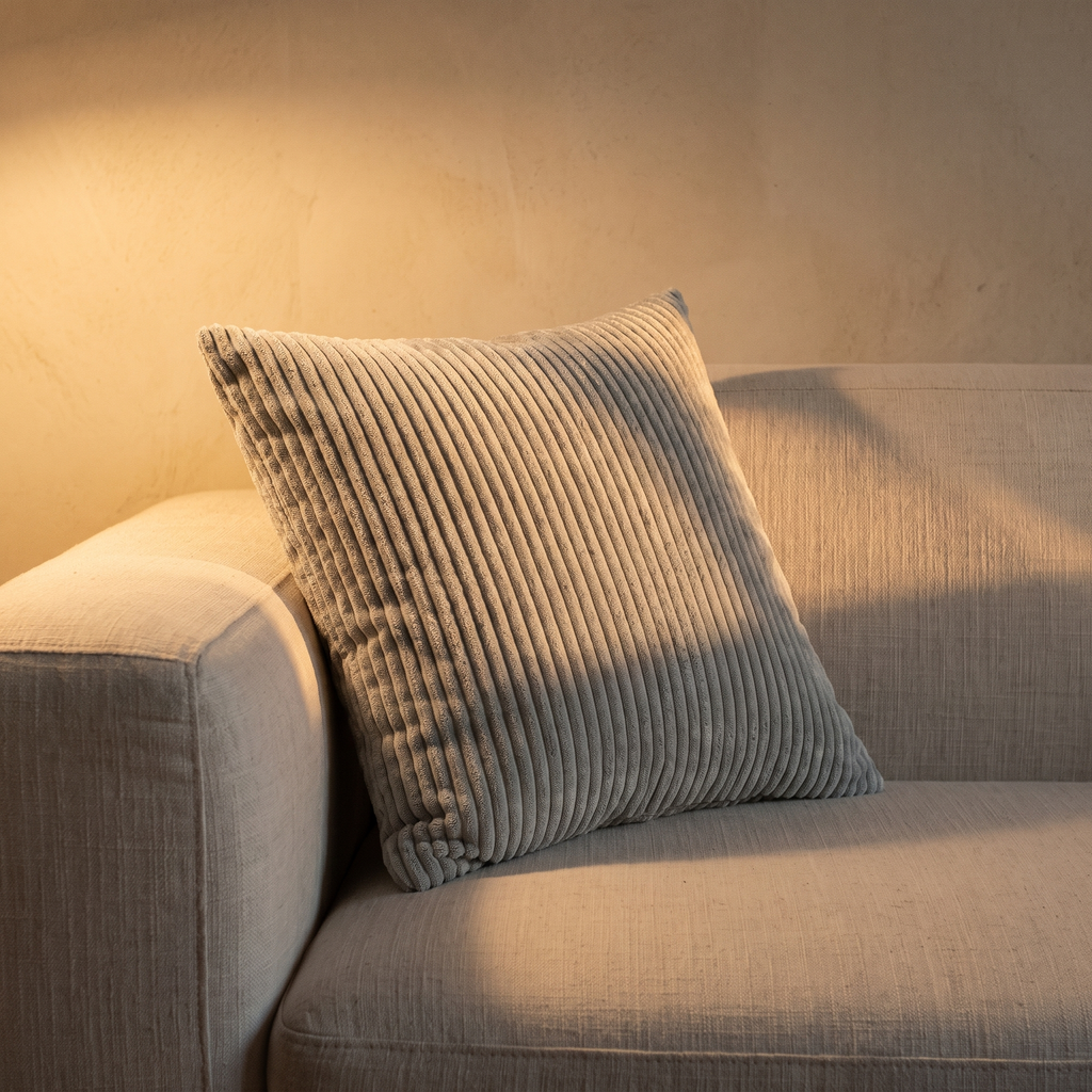Cojín de pana gris plata en ambiente de salón con luz cálida