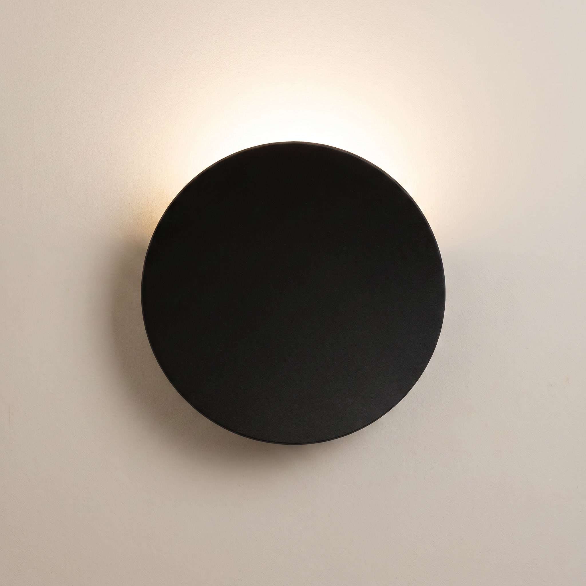 Aplique de pared LED redondo negro encendido sobre pared clara